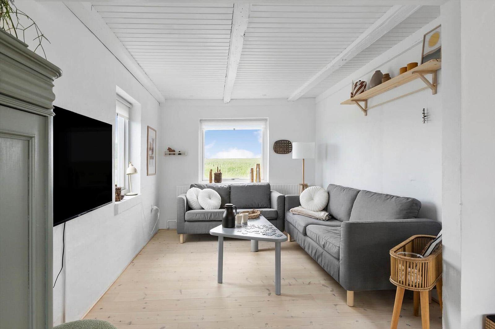 Wohnzimmer mit grauen Sofas, Holzboden und Fenster zum Grasfeld.