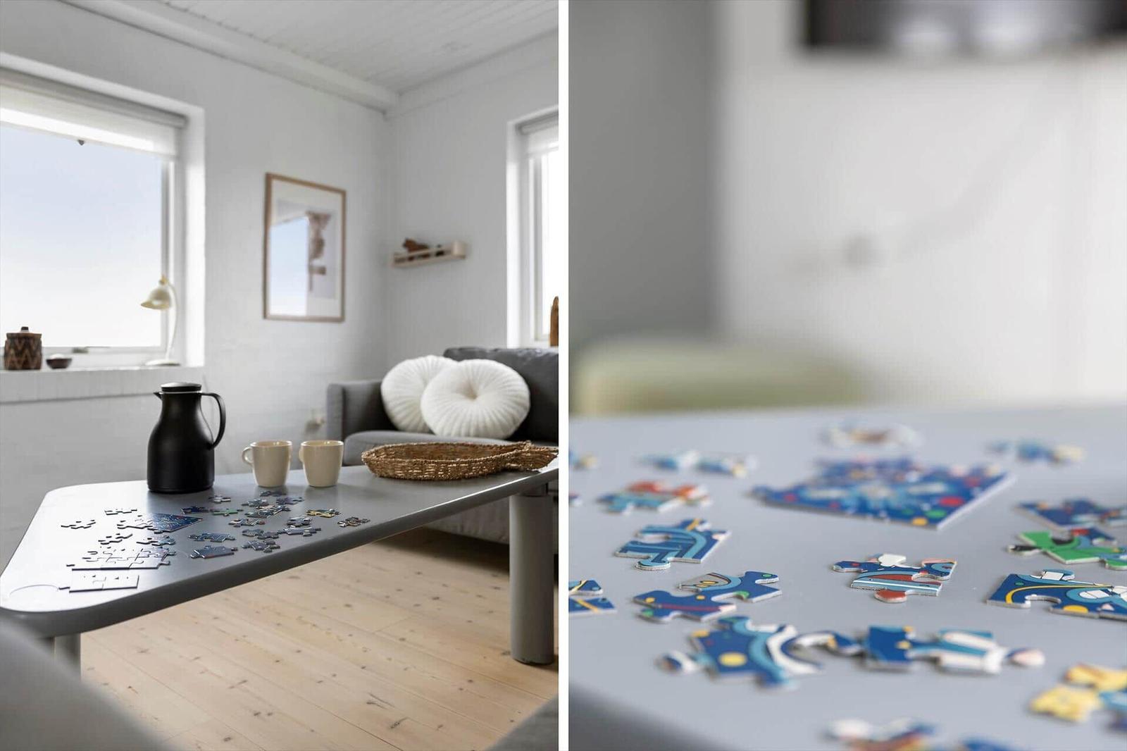 Ein Wohnzimmer mit einem Tisch, auf dem Puzzleteile liegen, und einem Sofa mit Kissen.