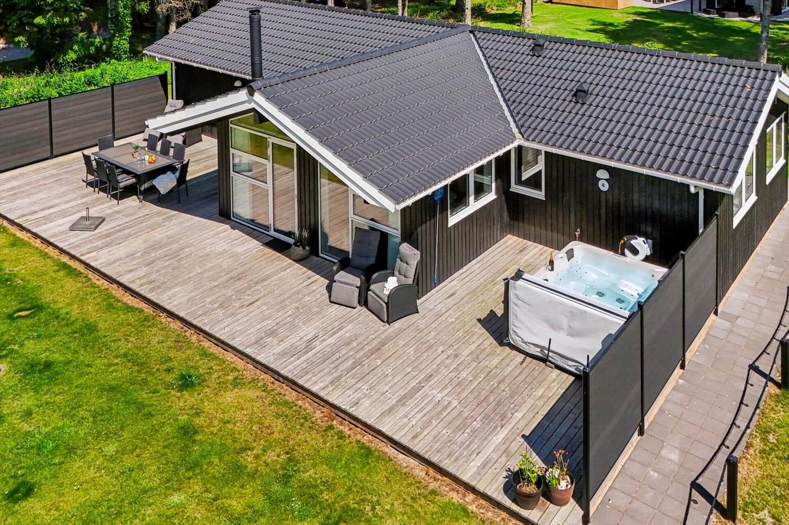 Haus mit großem Holzdeck, Whirlpool und Sitzgelegenheiten im Garten.