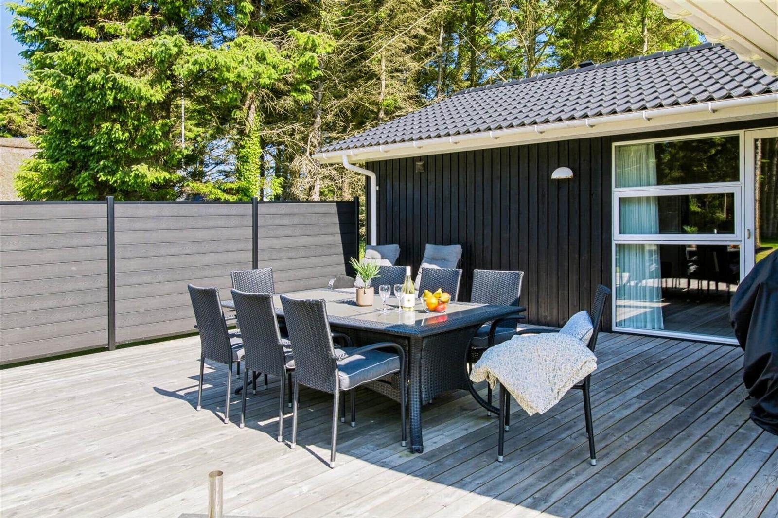 Terrasse mit Esstisch und Stühlen, angrenzend an ein Haus mit dunkler Fassade.