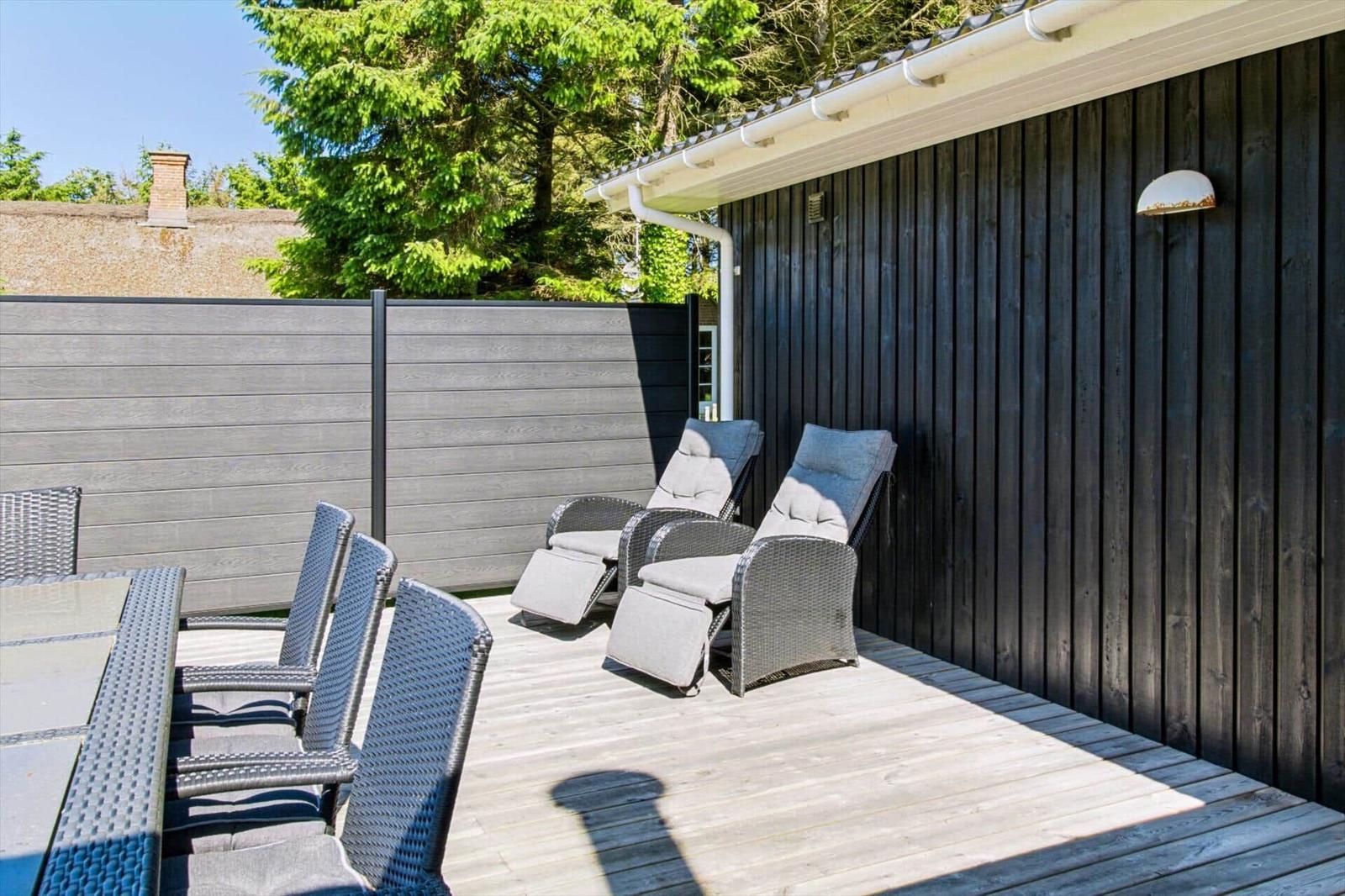 Terrasse mit Loungemöbeln und Tisch, umgeben von Holzwänden und einem Zaun.