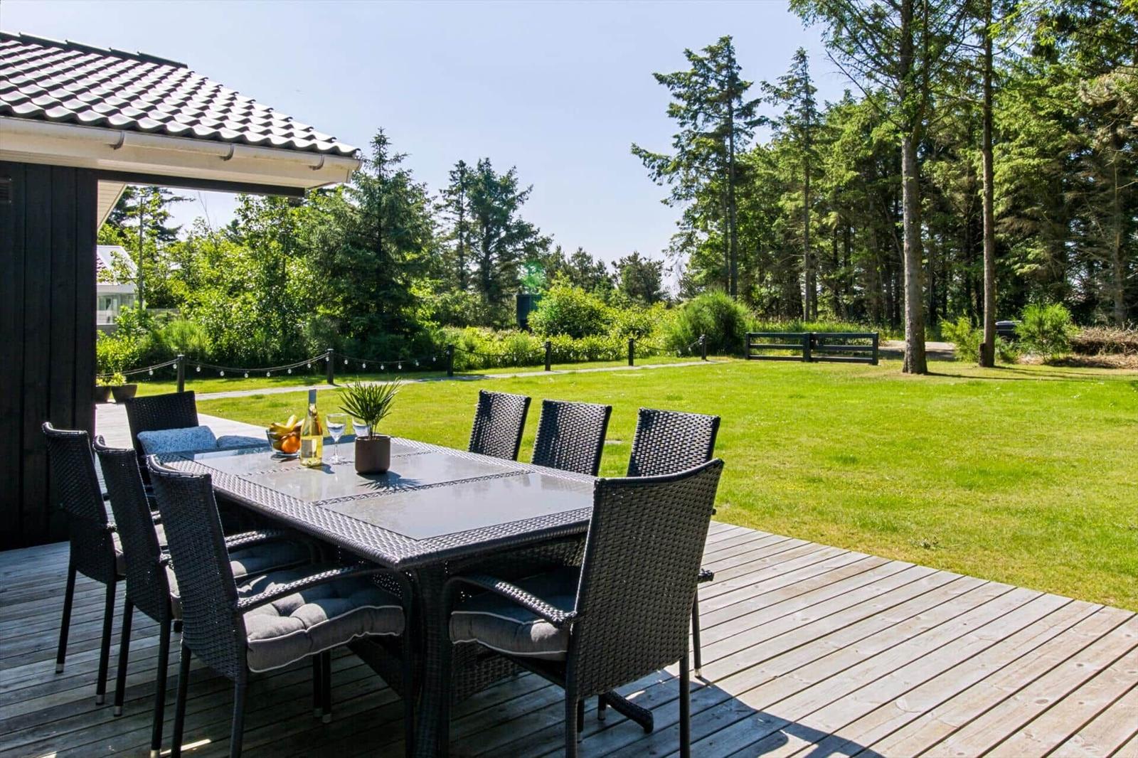 Terrasse mit Tisch und Stühlen, Grünfläche und Wald im Hintergrund.
