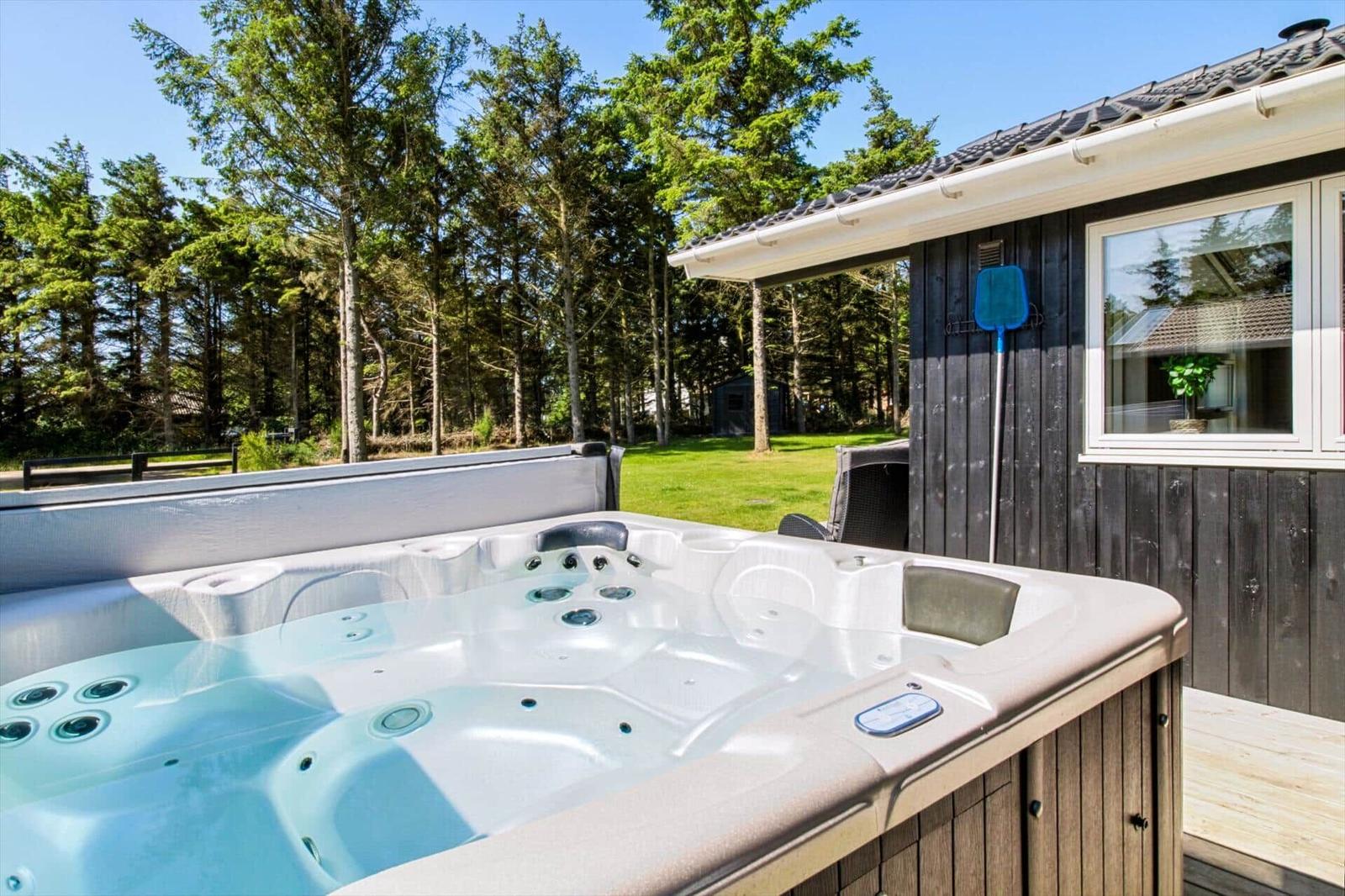Eine Whirlpoolbadewanne auf einer Terrasse neben einem Haus mit Wald im Hintergrund.