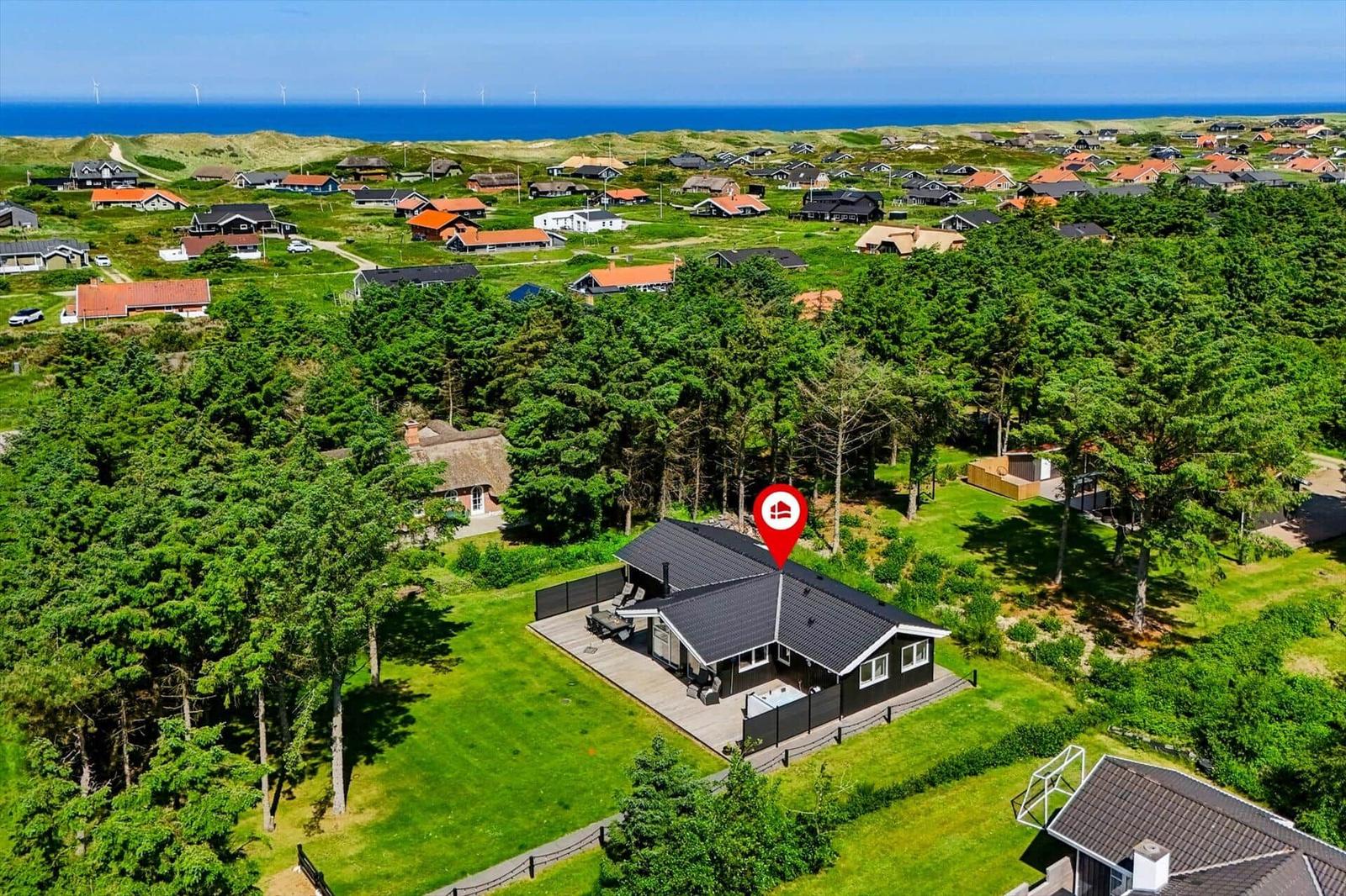 Moderne Villa mit Terrasse, umgeben von Grün und Bäumen, Blick auf das Meer und Windkraftanlagen.