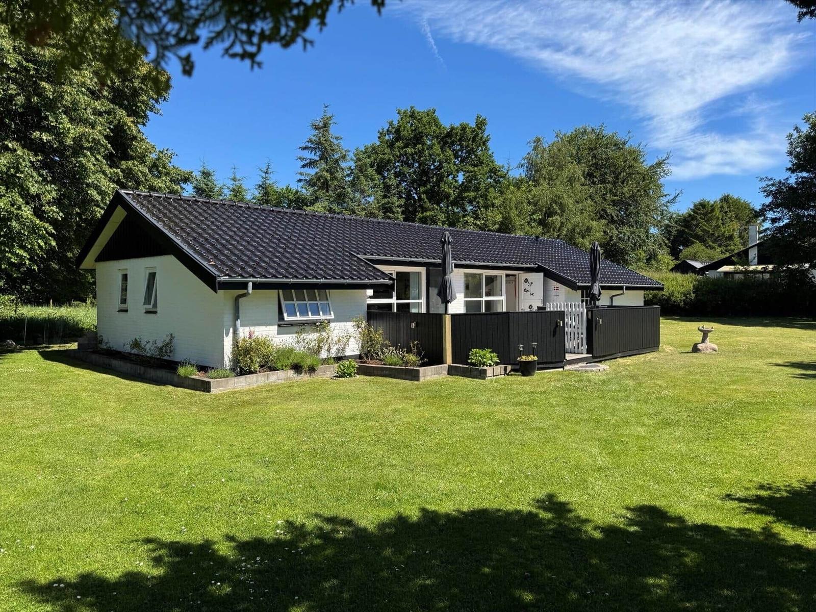 Ein weißes Haus mit schwarzem Dach und Garten. Zwei Sonnenschirme stehen auf der Terrasse.