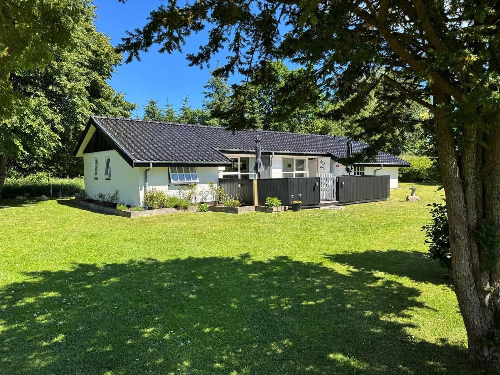 Ein weißes Haus mit dunklem Dach und Garten. Umgeben von Bäumen und Gras.