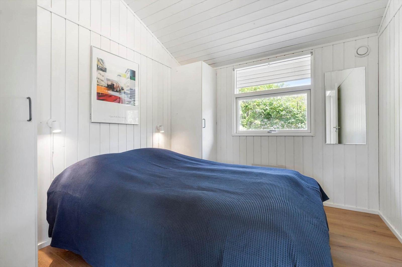 Schlafzimmer mit blauer Bettdecke, Fenster und Spiegel an der Wand.