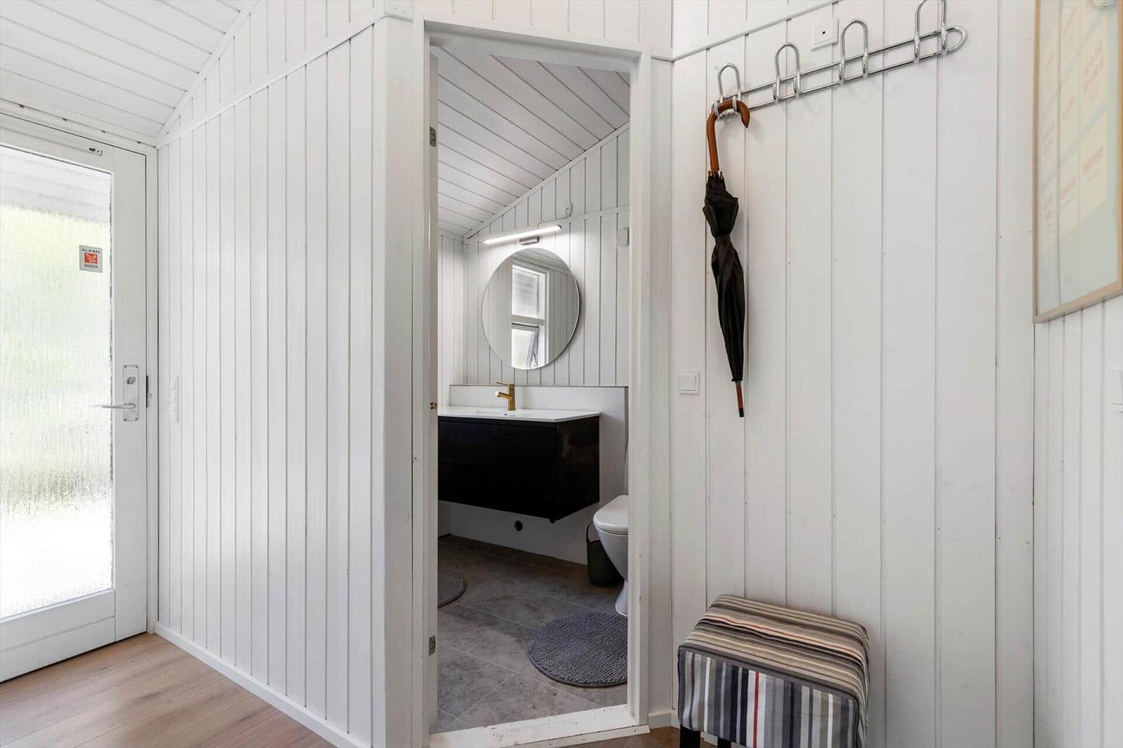 Badezimmer mit runder Spiegel, schwarzer Waschbeckenkonsole und Toilette. Regenmantel hängt an Wandhalter.