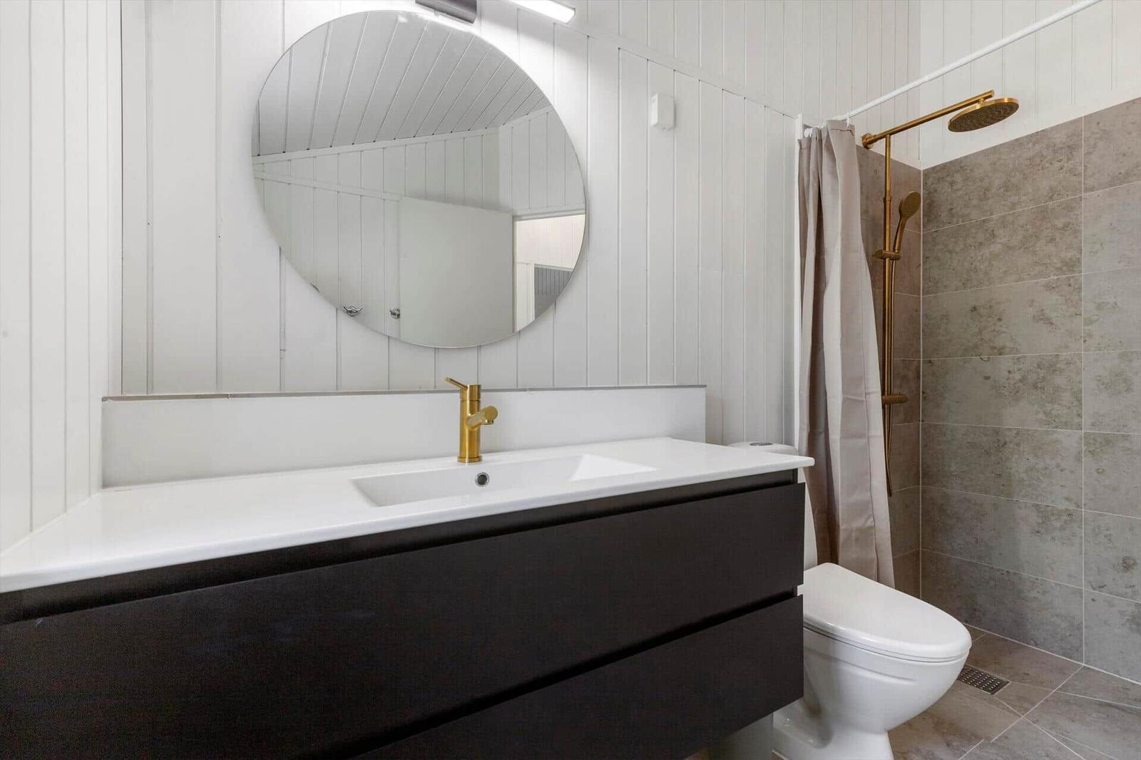 Badezimmer mit Waschtisch, Spiegel, Dusche und Toilette.