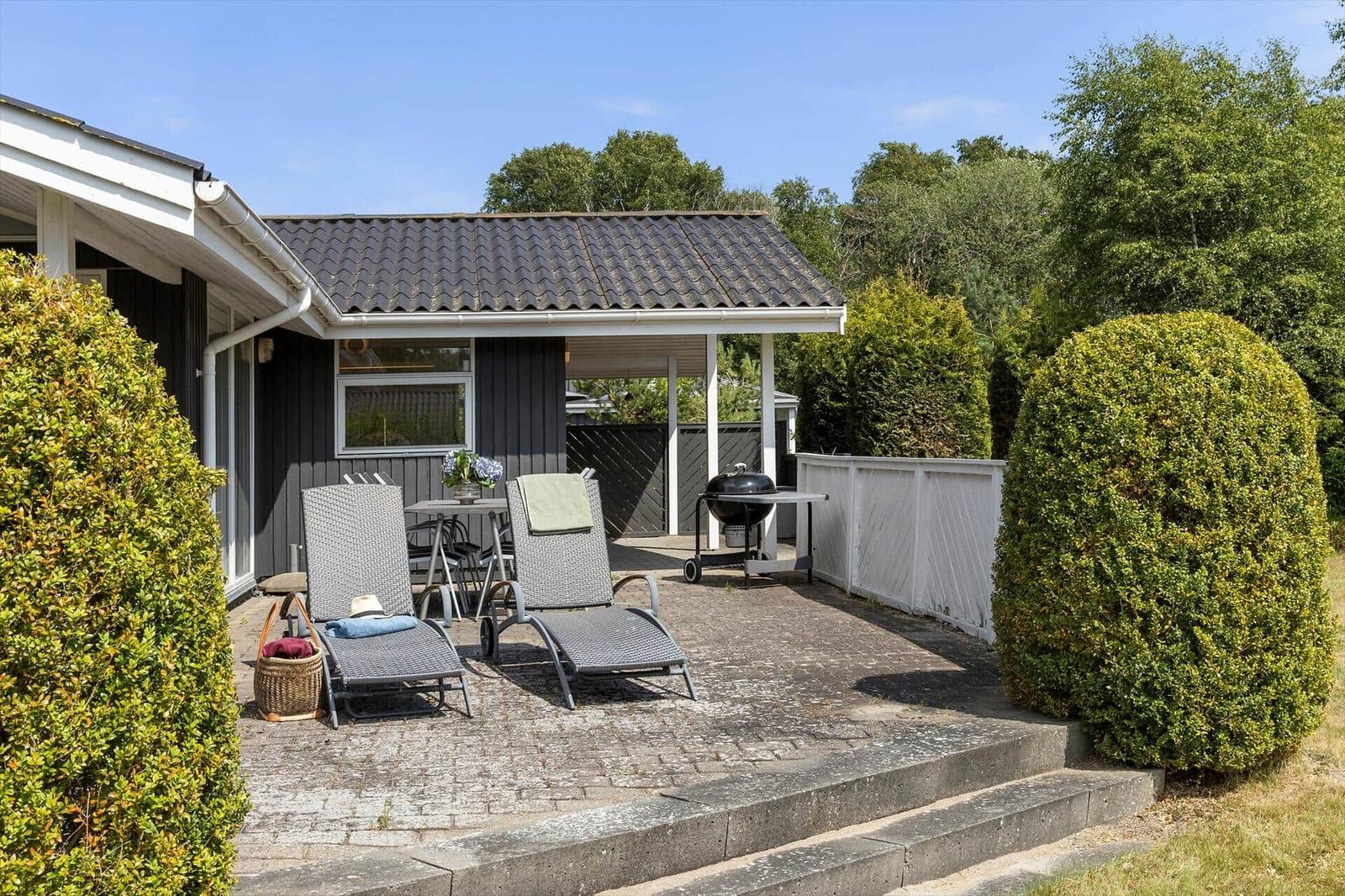 Terrasse mit Liegestühlen, Grill und Tisch. Hinterhof mit Hecken und Zufahrt.