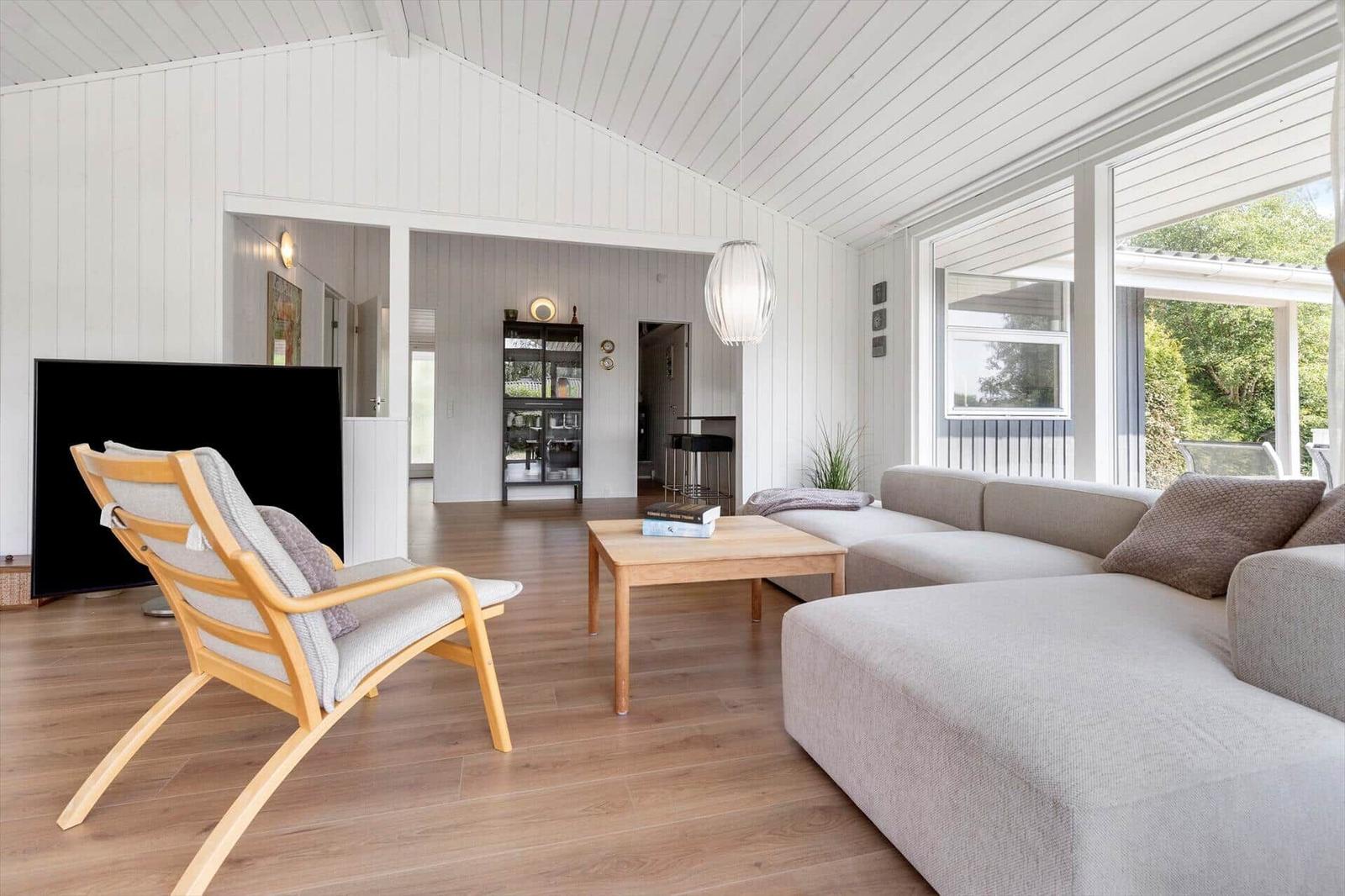 Wohnzimmer mit Sofa, Holzstuhl und Fernseher. Holzfußboden und weiße Wände.