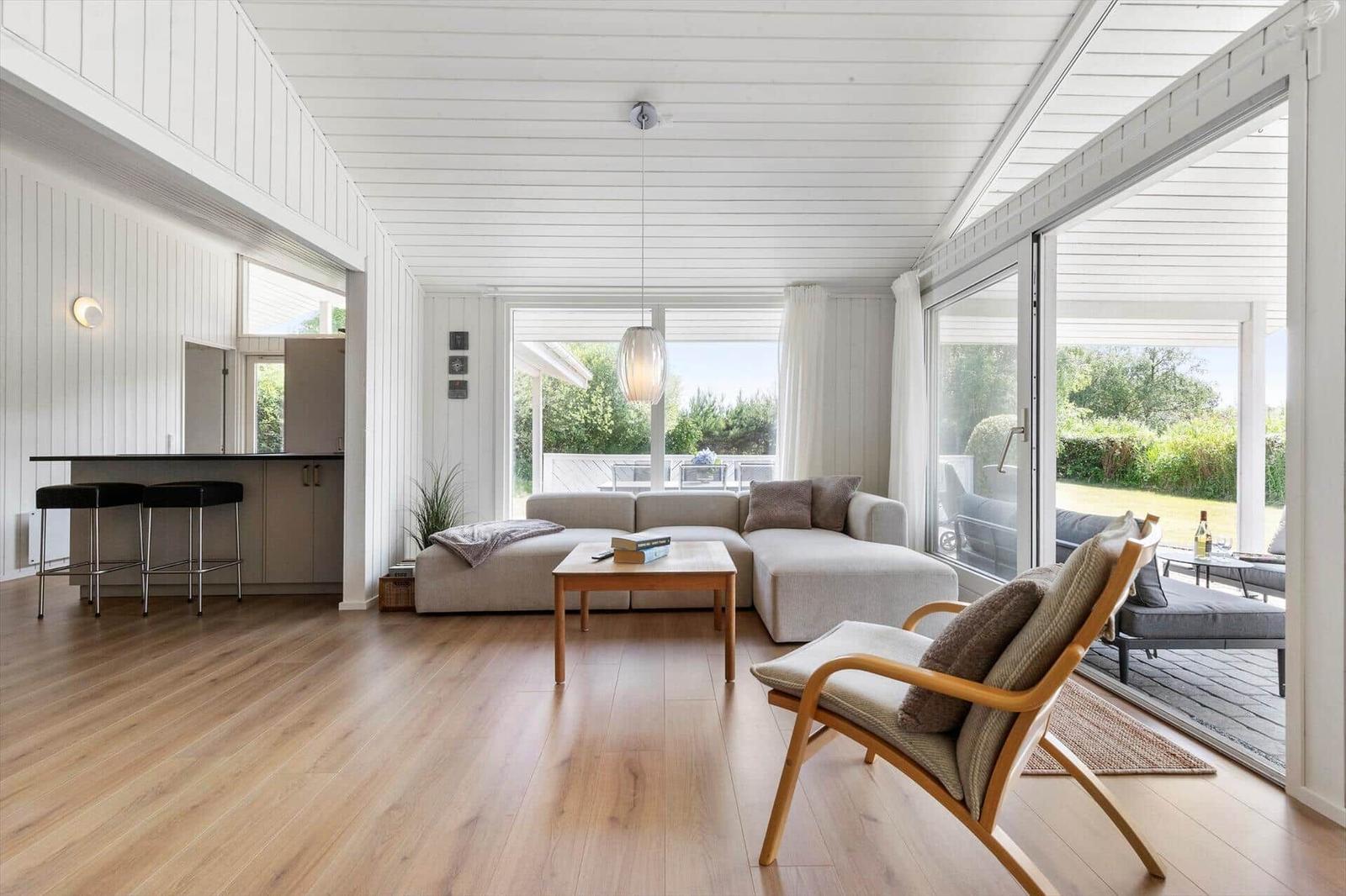 Wohnraum mit Sofa, Sessel und Holzboden. Durchgang zur Küche und Terrasse.