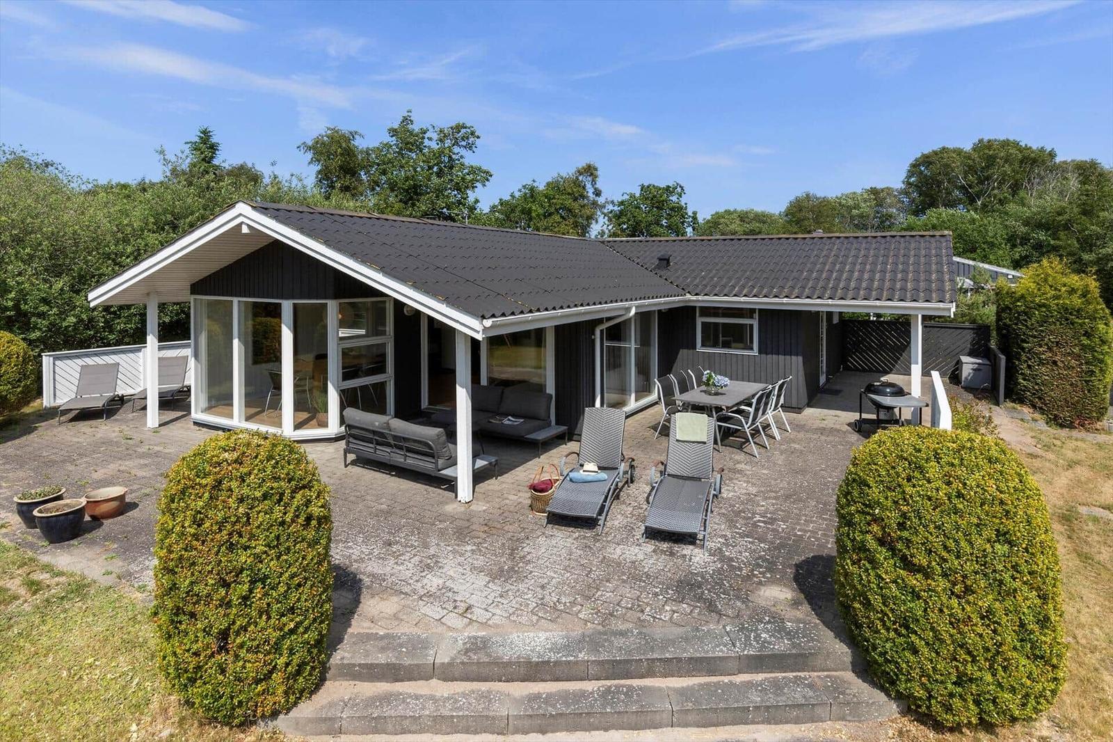 Ein Haus mit Terrasse, Gartenmöbeln und Grillplatz. Umgeben von Bäumen und Sträuchern.