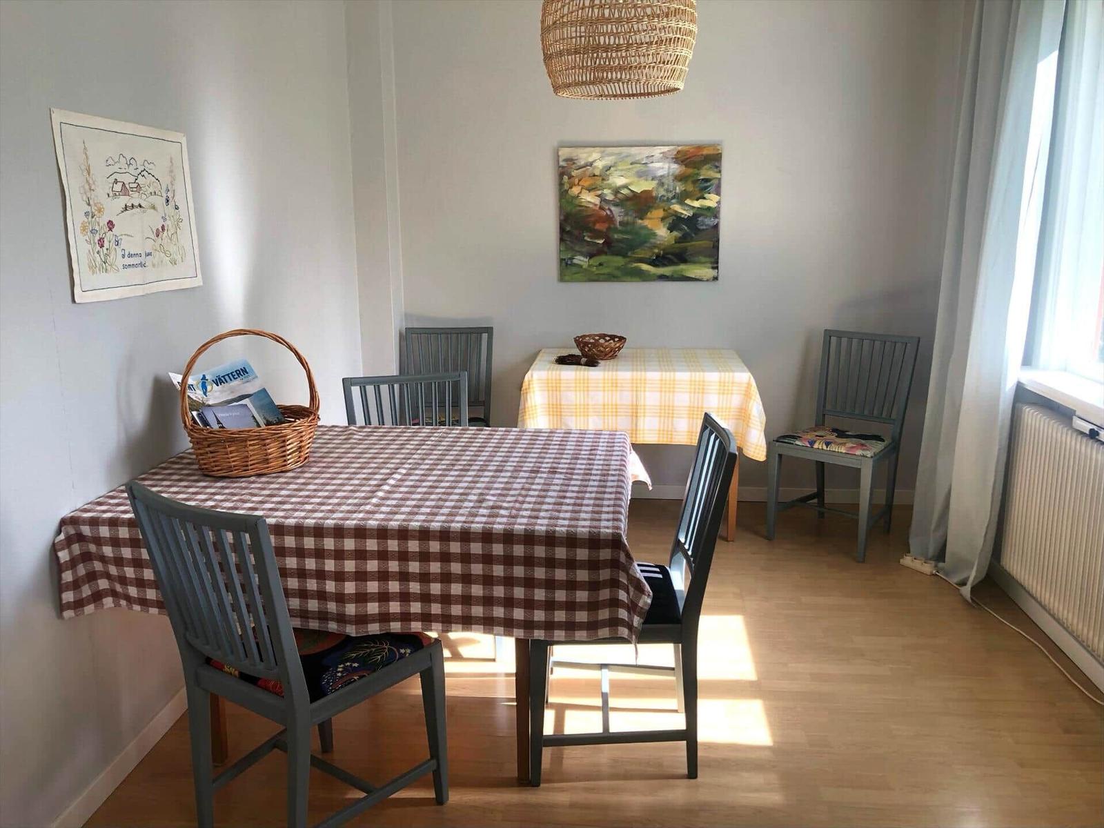 Esszimmer mit Tisch, Stühlen und Wandbildern. Fenster und Deckenleuchte sichtbar.