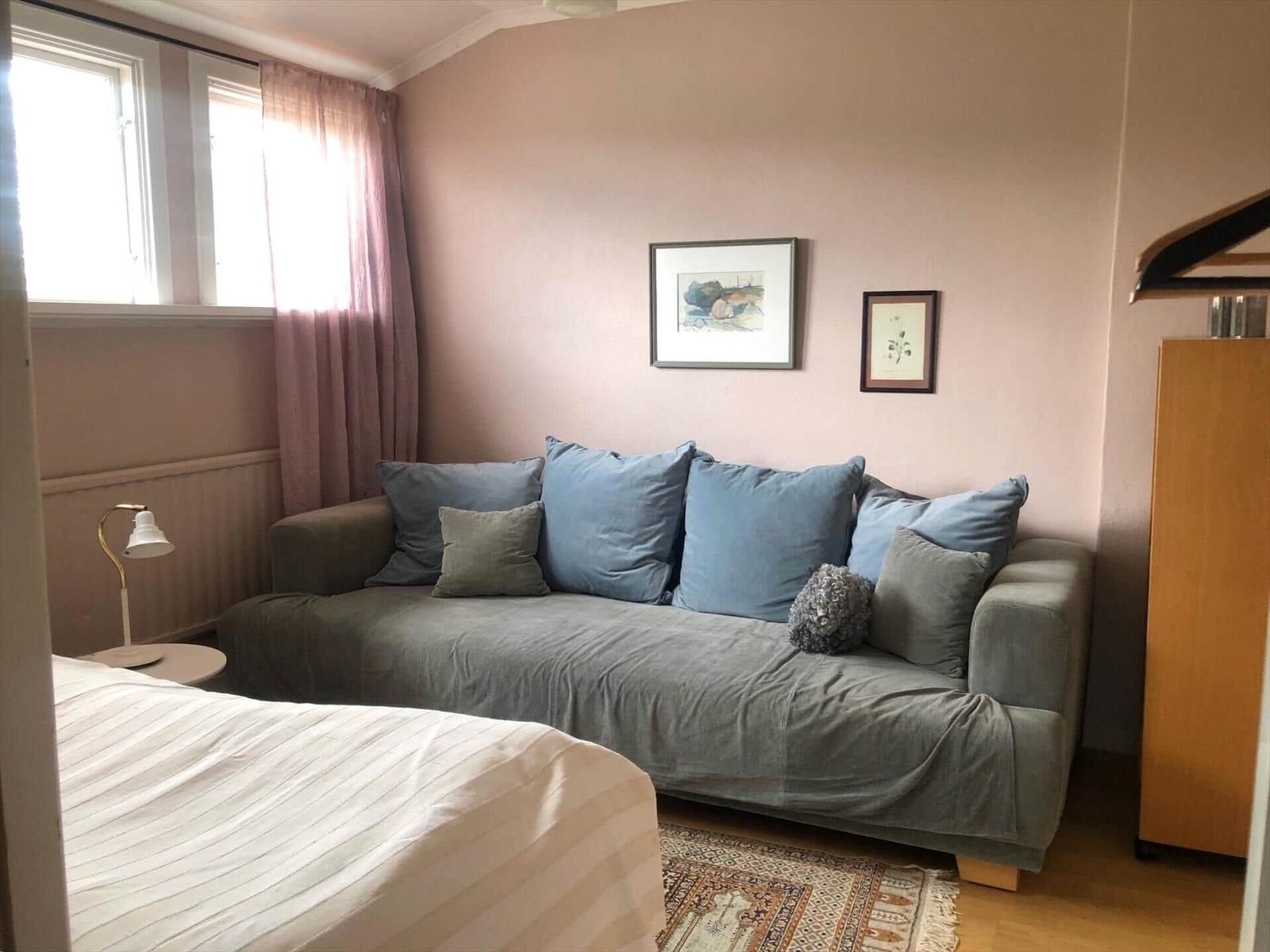 Ein Raum mit Sofa, Bett, Fenster und Wandbildern.