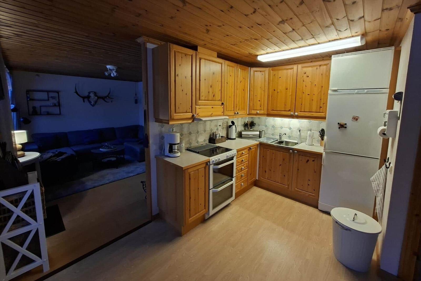 Küche mit Holzmöbeln, Kühlschrank und Blick in Wohnzimmer mit Sofa.