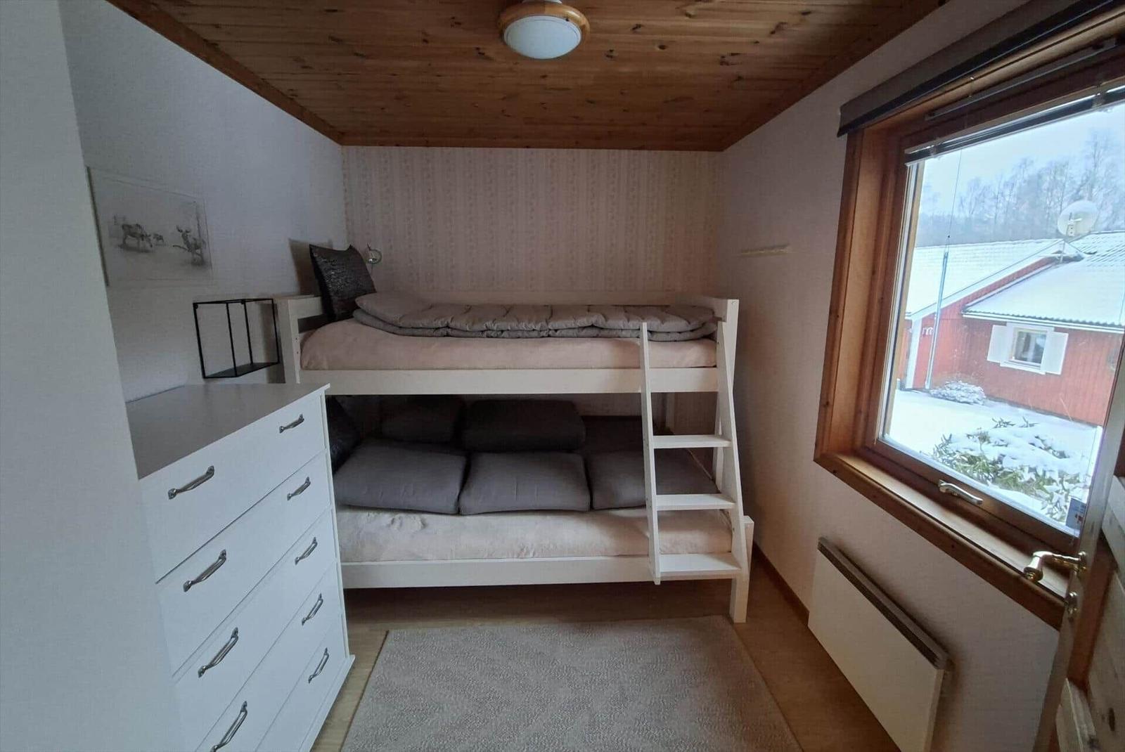 Zimmer mit Doppelstockbett, Schrank und Fenster mit Blick auf Haus und Schnee.