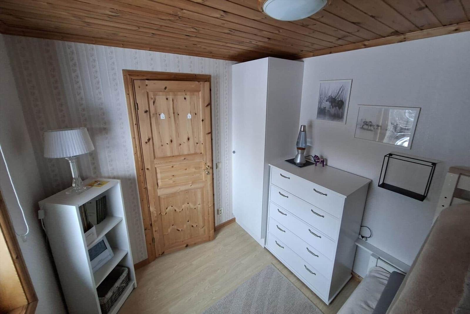 Schlafzimmer mit Holzboden, weißen Schränken und Holztür. Decke aus Holz, Wandbilder und Lampe.