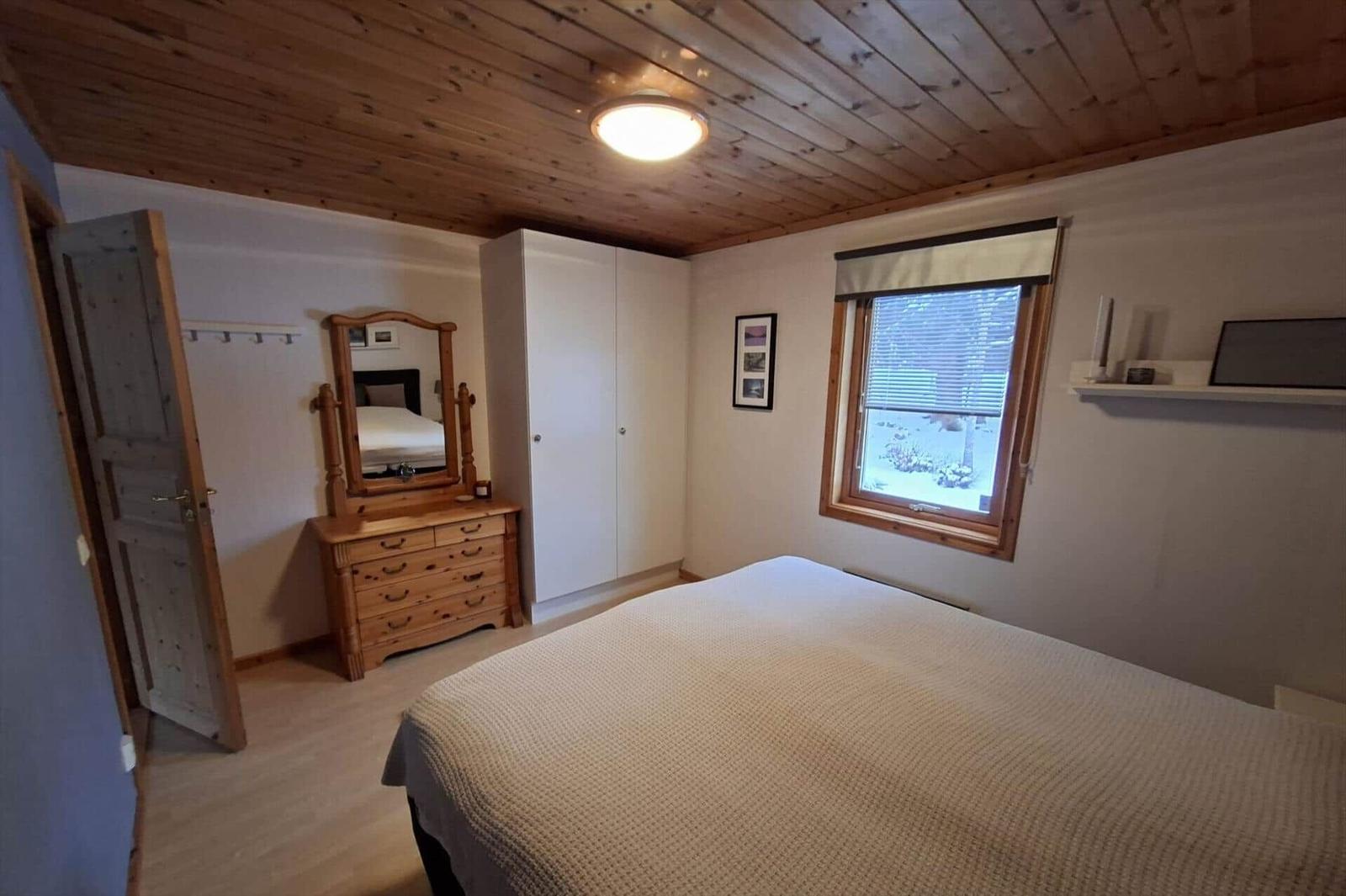 Schlafzimmer mit Holzdecke, Bett, Kleiderschrank und Fenster mit Blick.