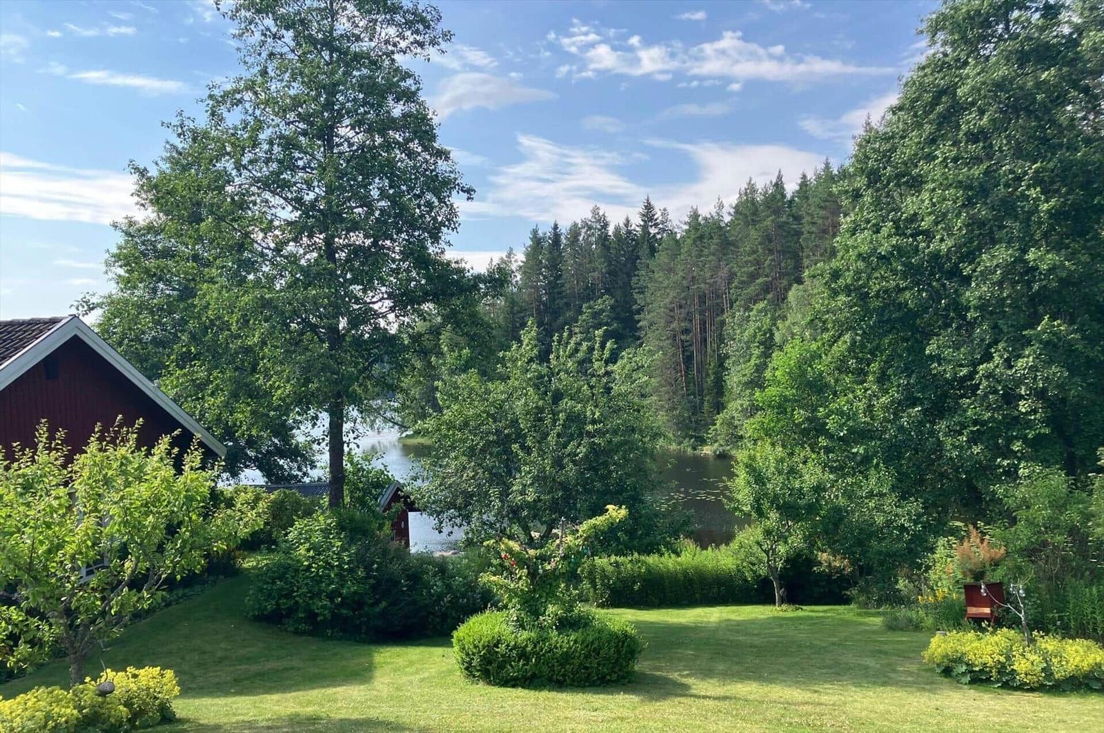 Roter Holzhaus mit Garten und Blick auf See und Wald.