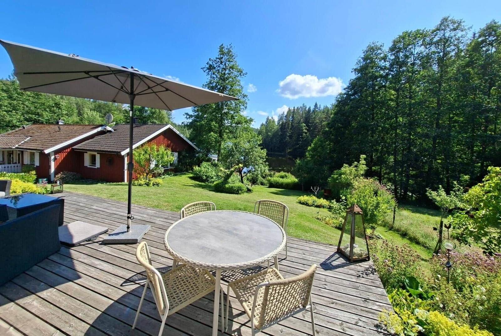 Terrasse mit Tisch, Stühlen und Sonnenschutz. Blick auf Garten und Wald.
