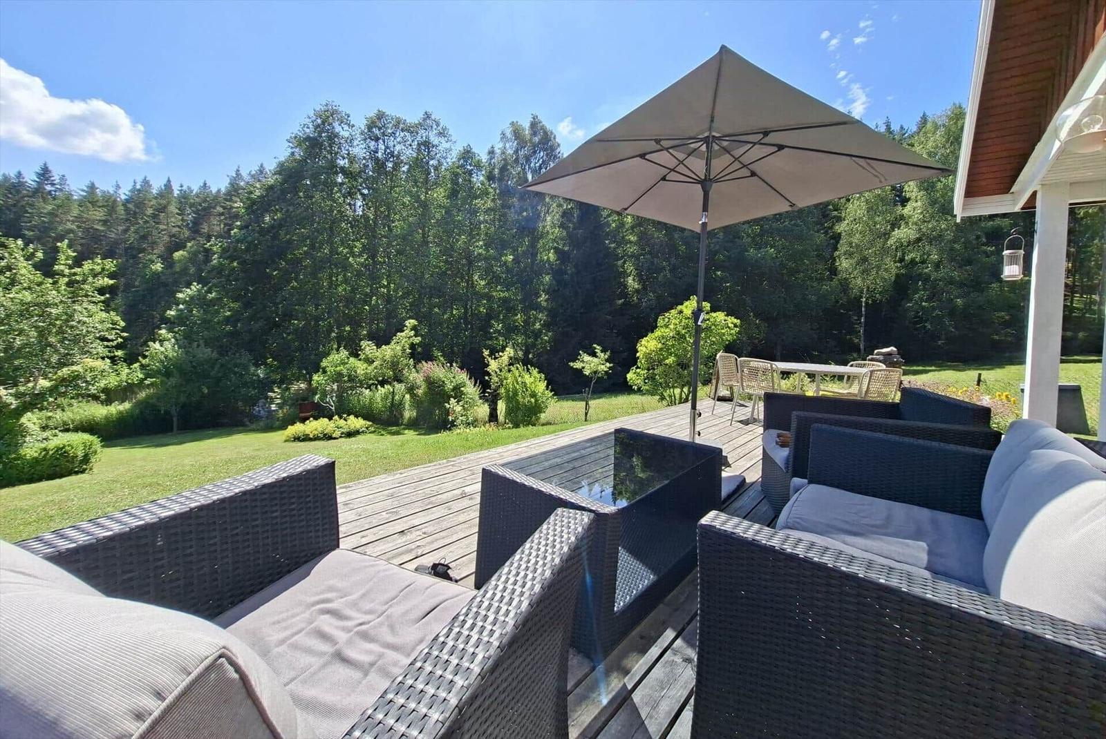 Terrasse mit Sitzgruppe, Sonnenschirm und Blick auf grünen Garten und Wald.