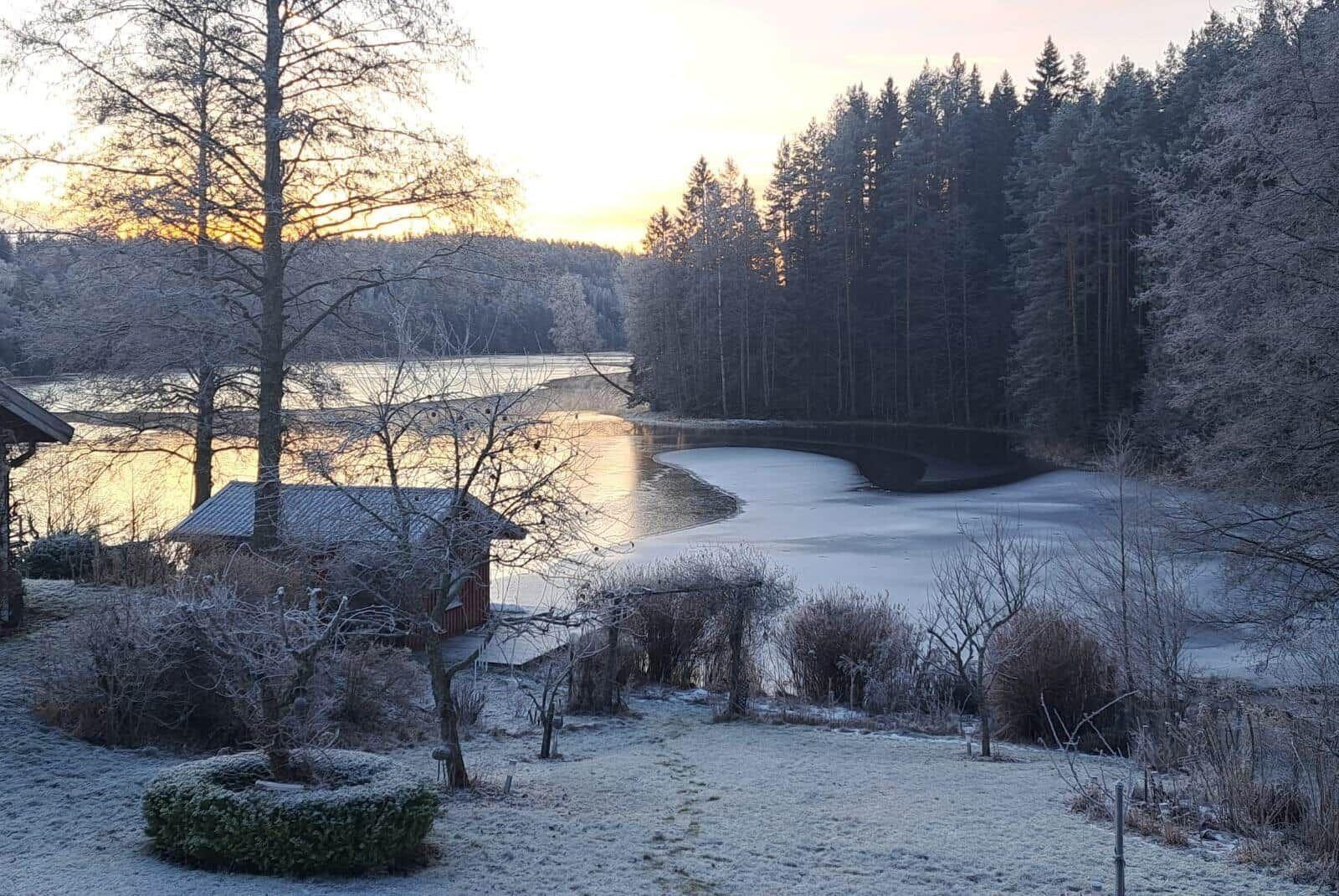Frosted lake with forest and small cabin at sunrise.