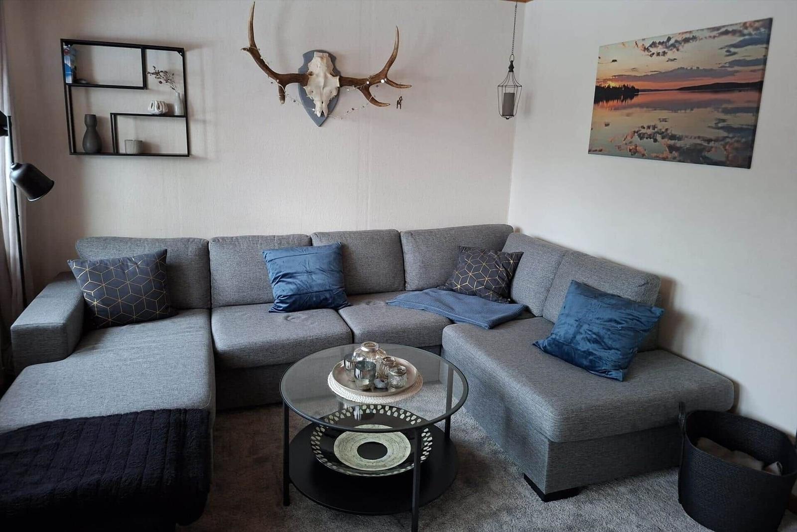 Grauer Ecksofa mit blauen Kissen und Glas-Tisch im Wohnzimmer.