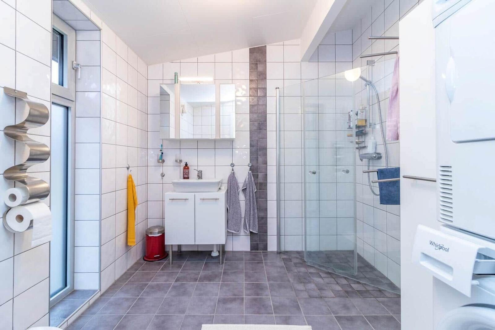 Badezimmer mit Dusche, Waschbecken und Toilette. Fliesen an den Wänden und Boden.