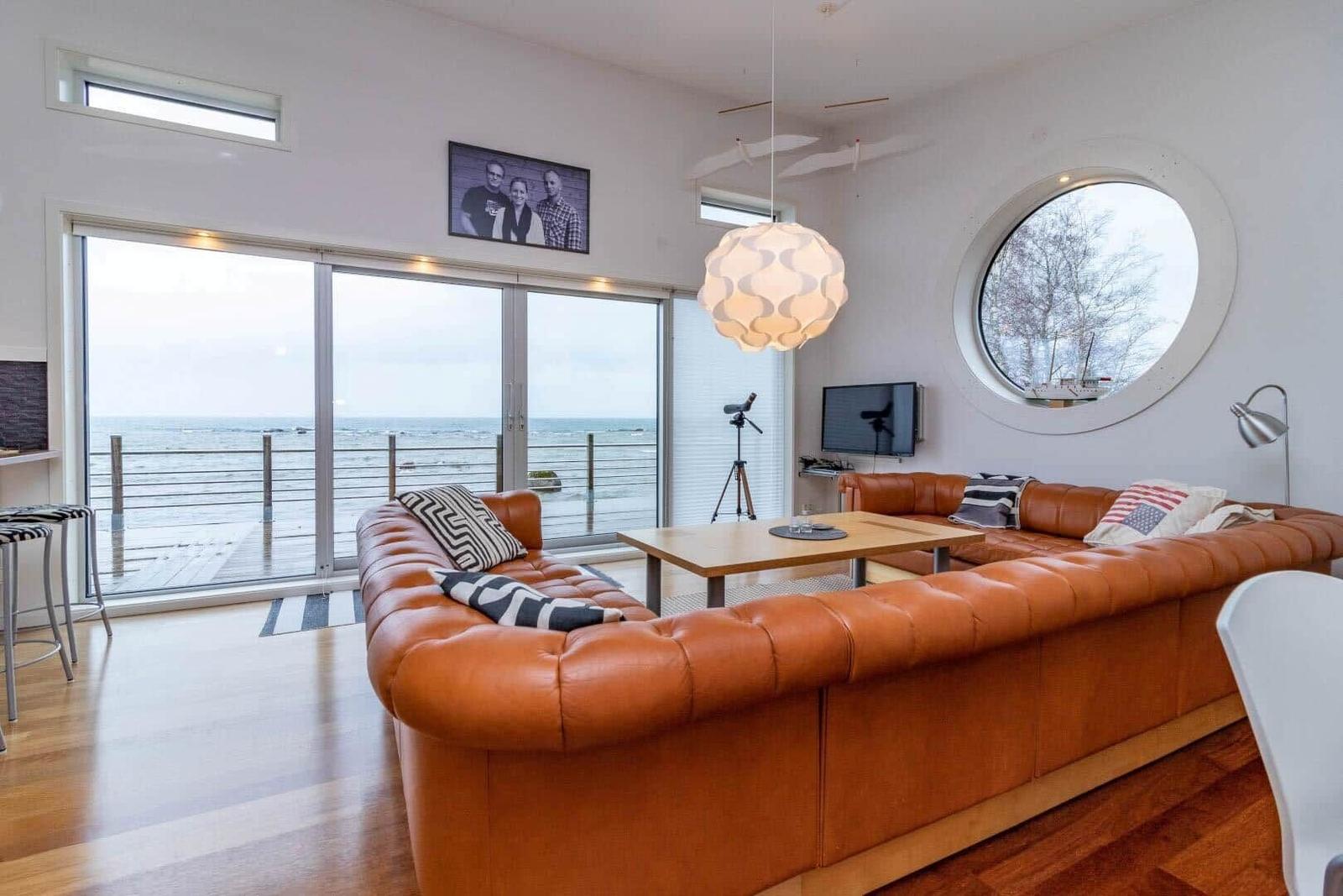 Wohnzimmer mit braunem Ledersofa, runden Fenster und Blick aufs Meer.
