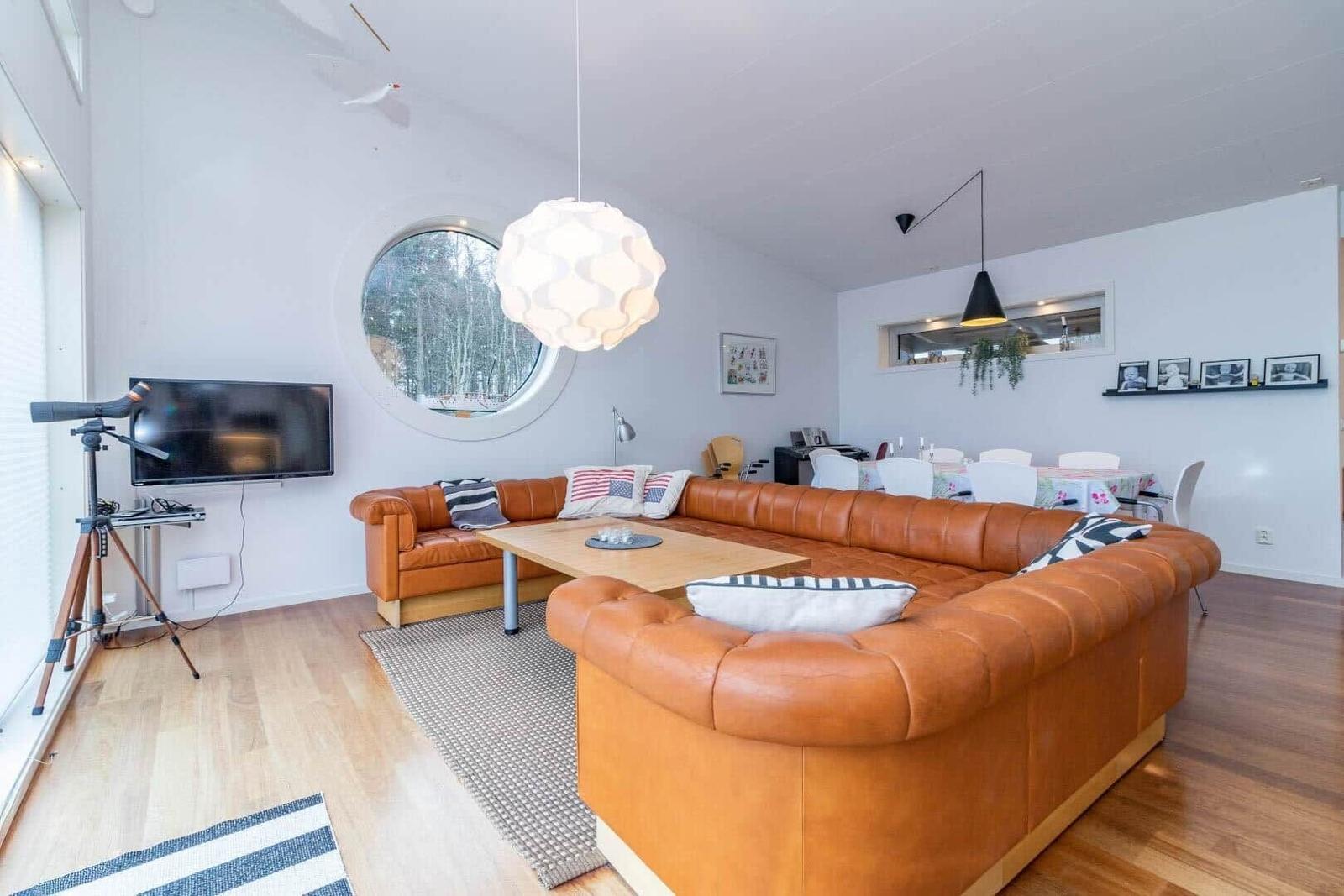 Wohnzimmer mit braunem Sofa, runden Fenster und Holzboden.
