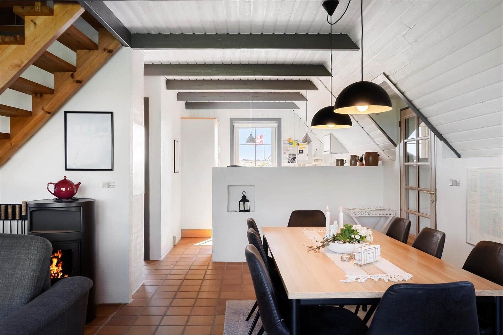 Essbereich mit Holztisch, Stühlen und Kamin. Holzstufen und weiße Wände.