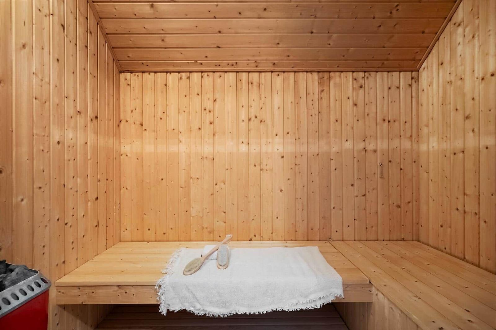Holzsauna mit Sitzbank, weißer Decke und Bürsten.