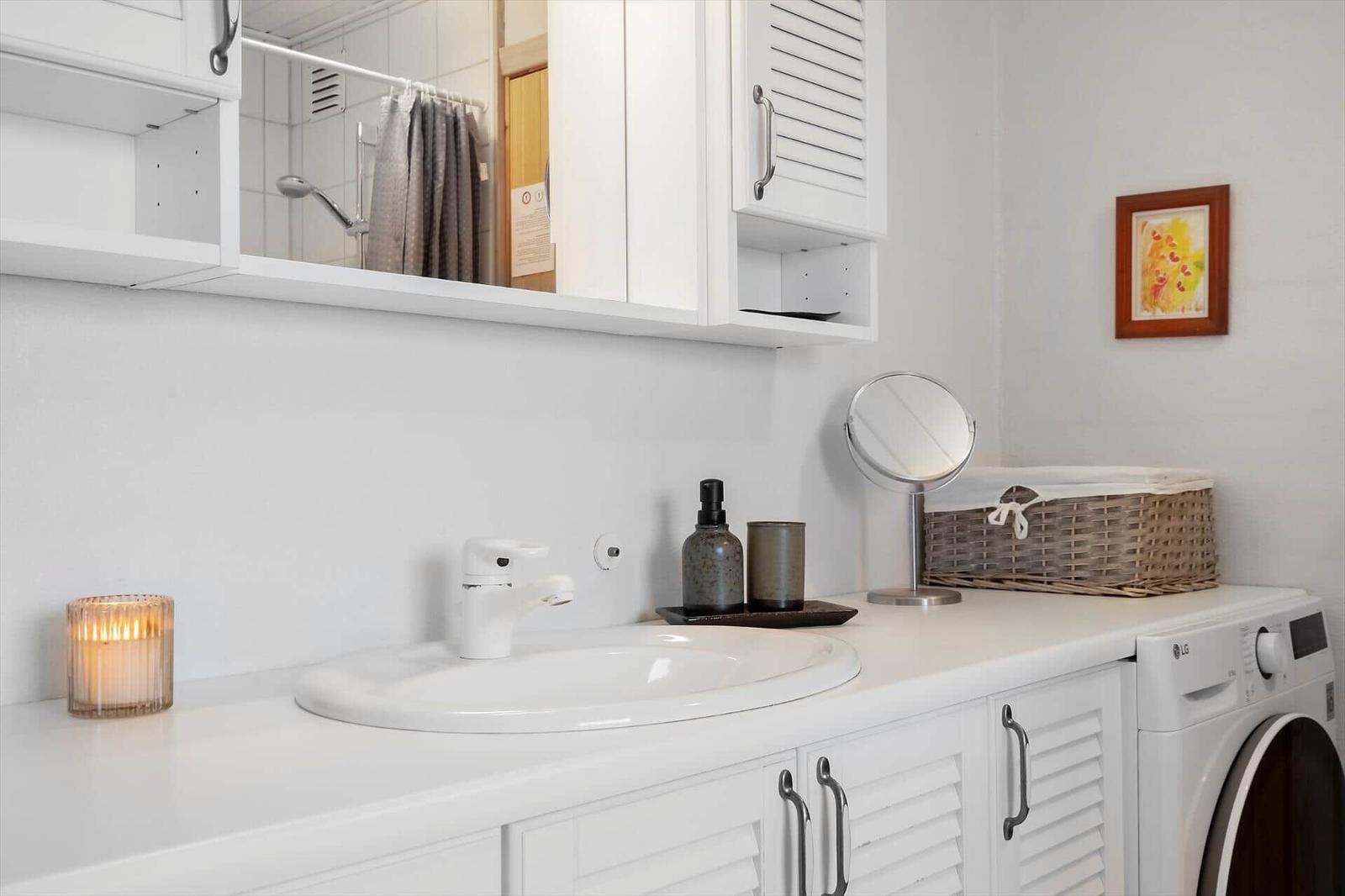 Waschbecken mit Spiegel, Waschmaschine und Badezimmer im Hintergrund.