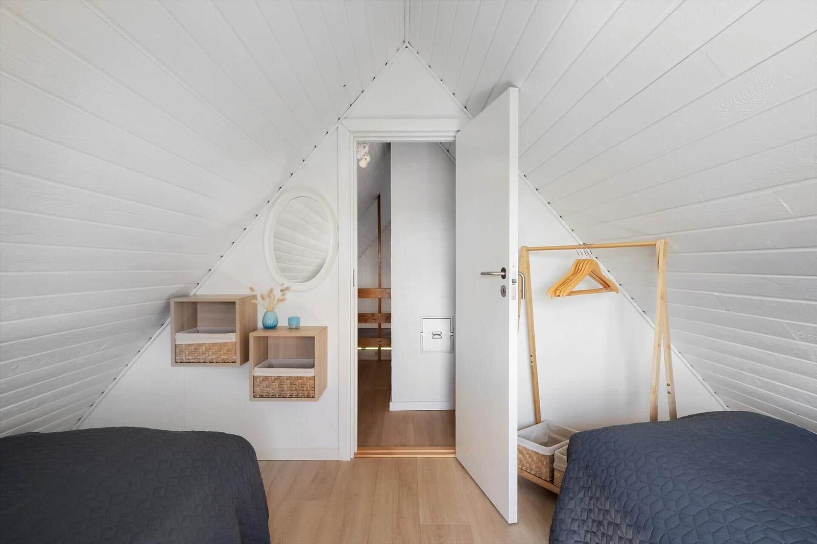 Zimmer mit zwei Betten, weißen Wänden und Holzboden. Tür führt in einen Flur.