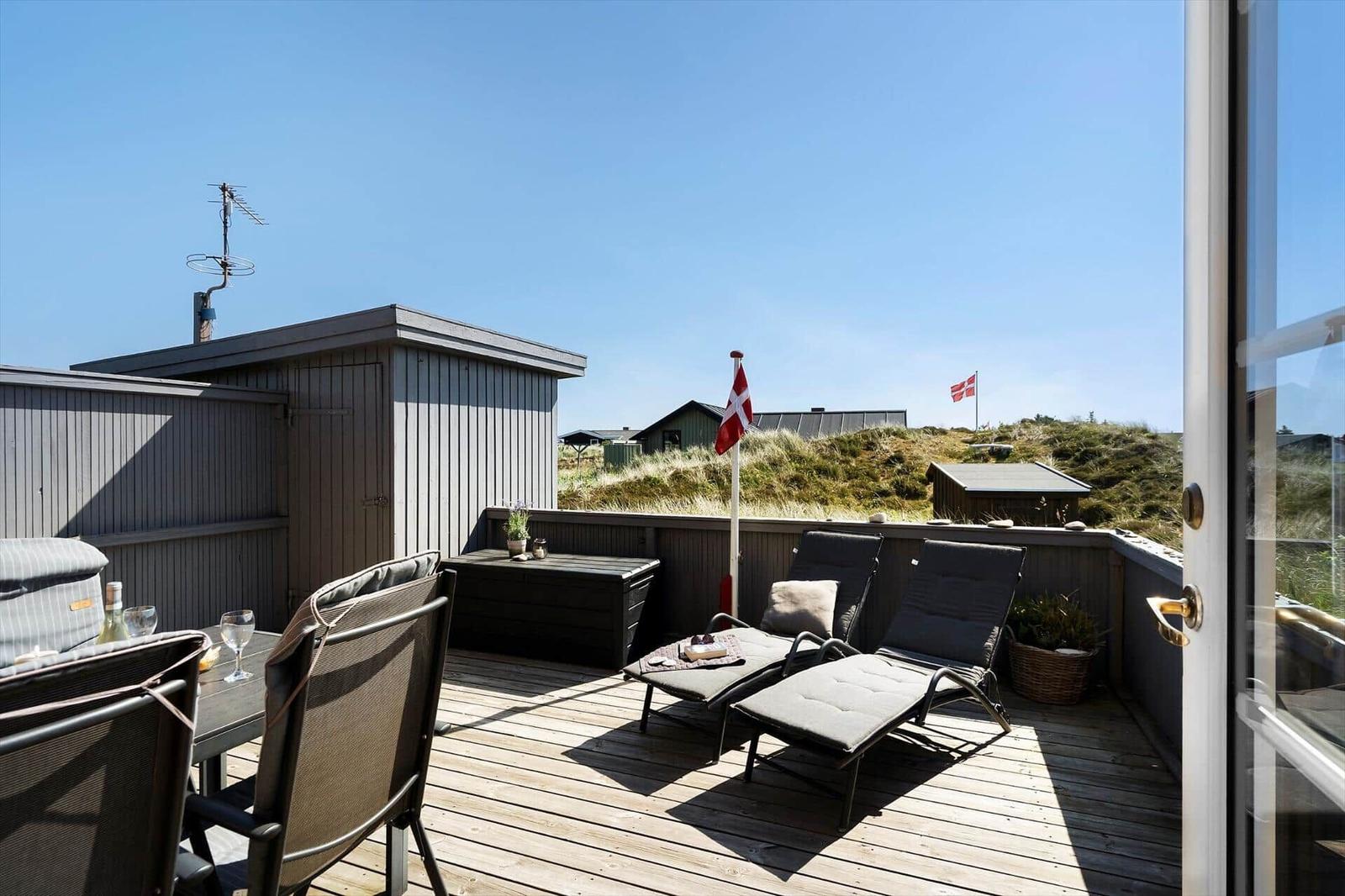 Terrasse mit Liegestühlen und Tisch. Blick auf Grasland und Flagge.