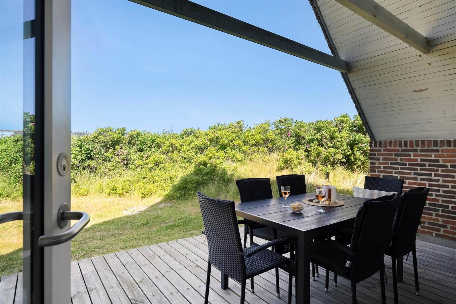 Terrasse mit Tisch und Stühlen, Blick auf grüne Landschaft unter blauem Himmel.
