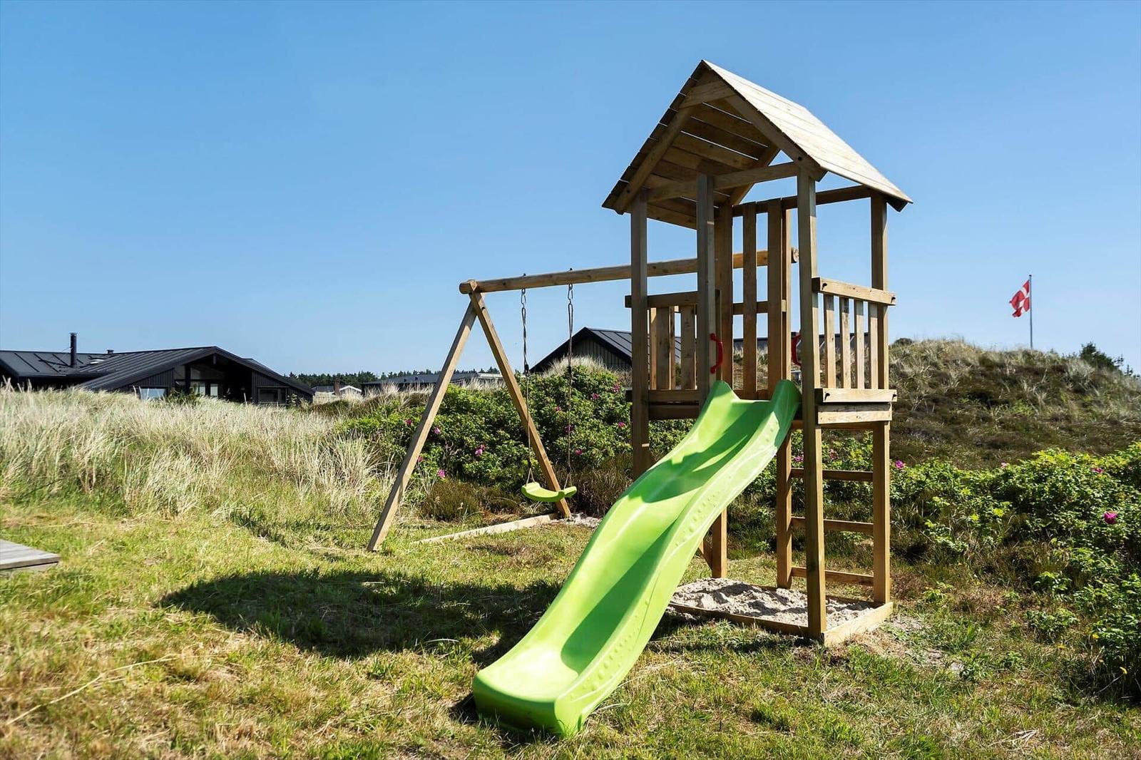 Holzspielplatz mit Rutsche und Schaukel auf grünem Rasen.