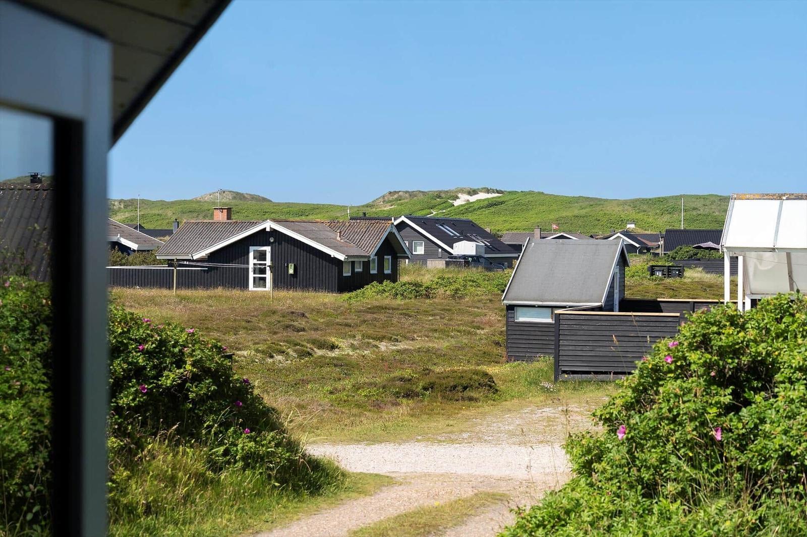 Ansicht von Ferienhäusern mit Grünflächen und Dünen im Hintergrund.