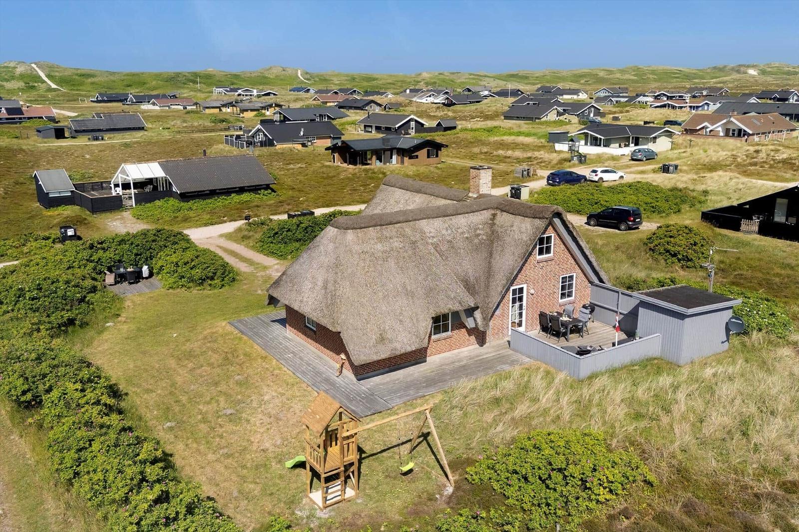 Haus mit Strohdach, Terrasse und Spielplatz auf grünem Grundstück