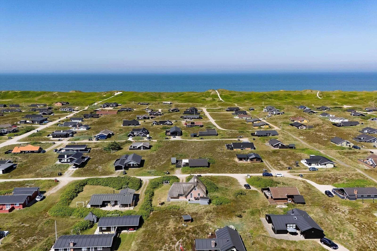 Aerial view of coastal holiday homes with green dunes and blue sea in the background.