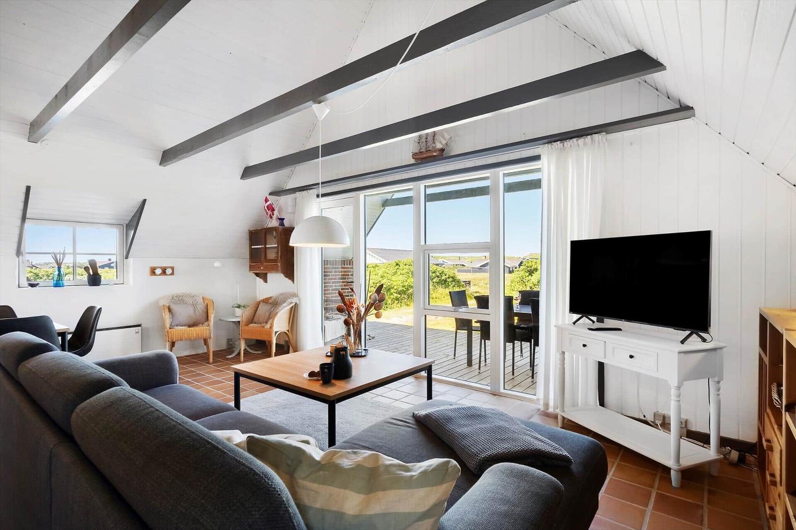 Wohnzimmer mit Sofa, TV und großem Fenster zum Balkon.