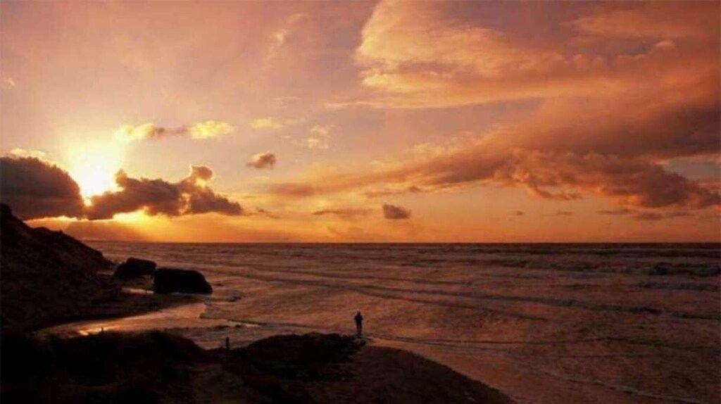 Sonnenuntergang am Meer mit Silhouette einer Person und Felsen