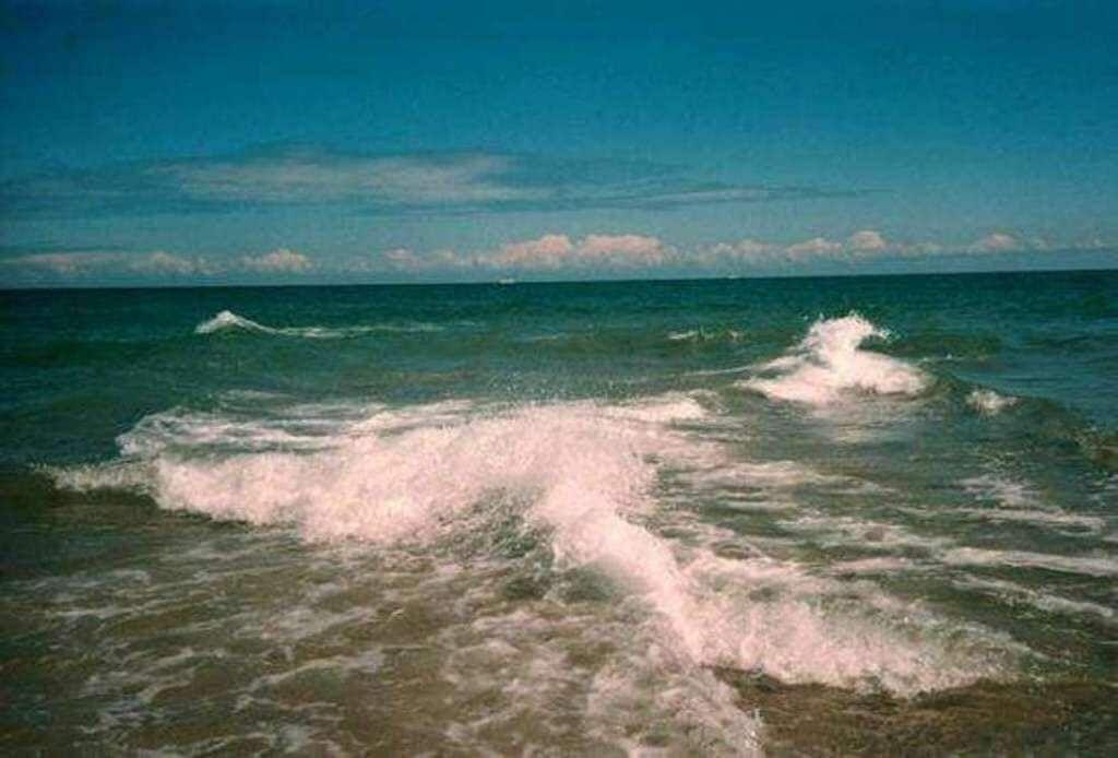 Wellen brechen am Strand. Der Himmel ist klar mit einigen Wolken.