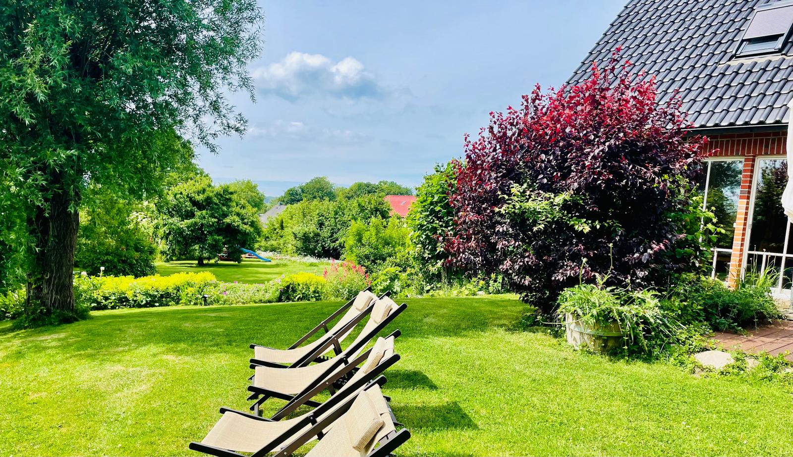 Grüner Garten mit Liegestühlen und Blick auf Wald und Haus.