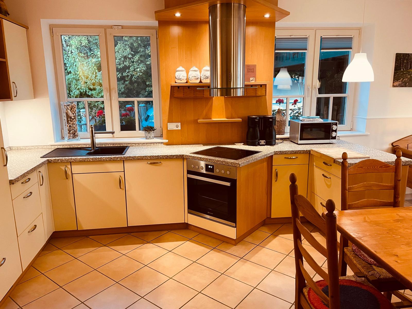 Küche mit Holzmöbeln, Edelstahlherd und Fenstern zum Garten