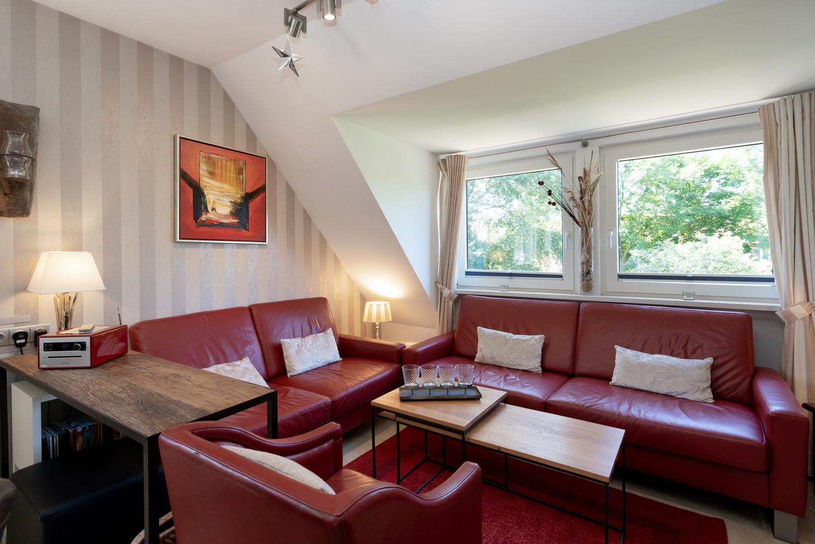 Wohnzimmer mit rotem Ledersofa, Holztisch und Fenster mit Blick auf Bäume.