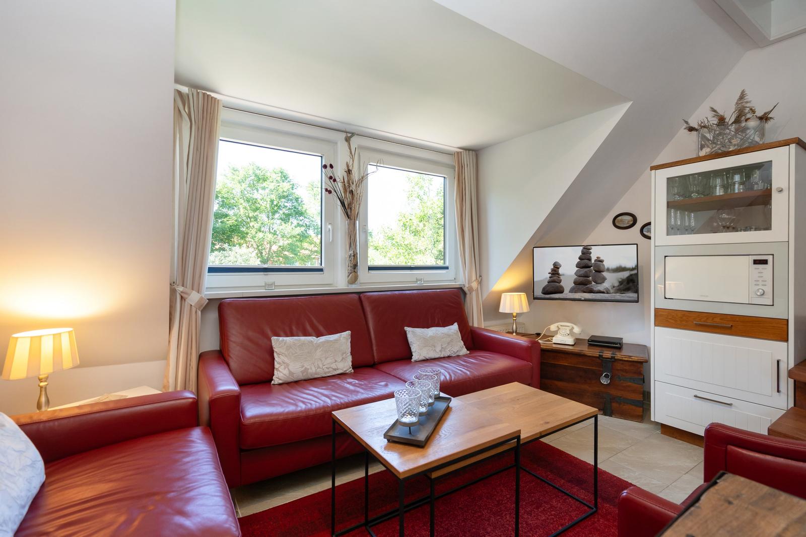Ein Wohnzimmer mit rotem Sofa, Holztisch und Fenstern zum Garten.
