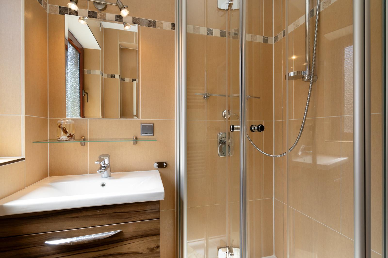 Badezimmer mit Dusche, Waschbecken und Spiegel.