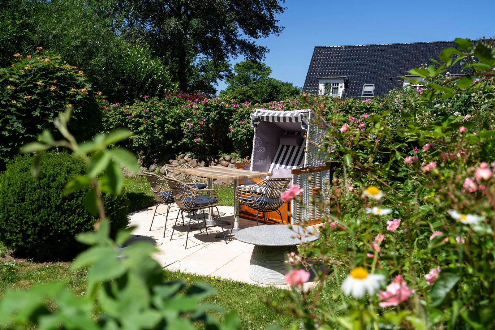 Garten mit Sitzgruppe, Strandkorb und Blumen. Hintergrund: Haus mit dunklem Dach.